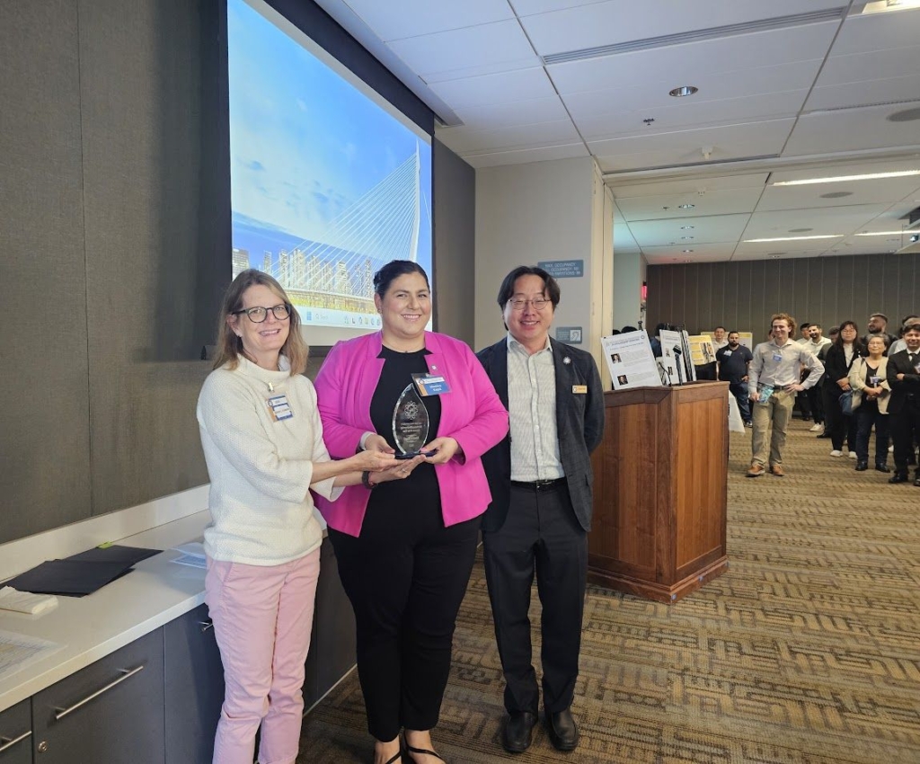 Photo of Kapil holding her award flanked by two faculty members