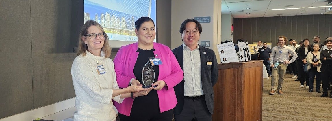 Photo of Kapil holding her award flanked by two faculty members