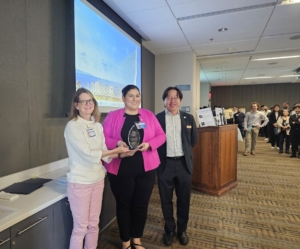 Photo of Kapil holding her award flanked by two faculty members